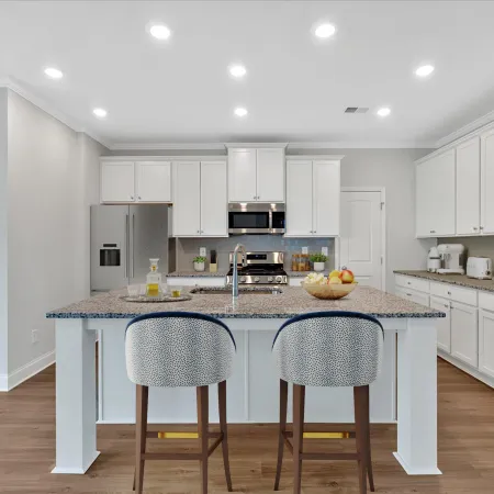 Bright modern kitchen with white cabinets, granite island, two patterned stools, stainless steel appliances, and wood floor.