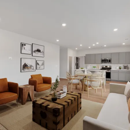 Modern open living room with brown armchairs, white sofa, wooden coffee table, dining area, and gray kitchen cabinets.