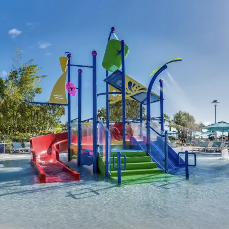 Colorful children's water play structure with slides, water buckets, and spraying water under a clear blue sky.