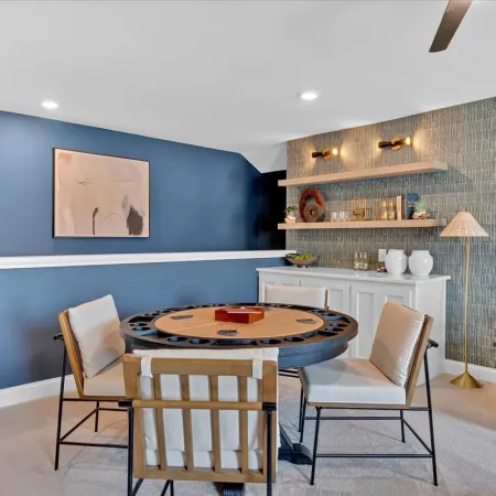 Modern game room with round card table, neutral chairs, blue accent wall, and stylish shelving with decor.