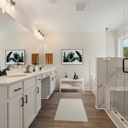 Bright modern bathroom with white cabinetry, dual sinks, glass shower, wooden floor, and tropical wall art.