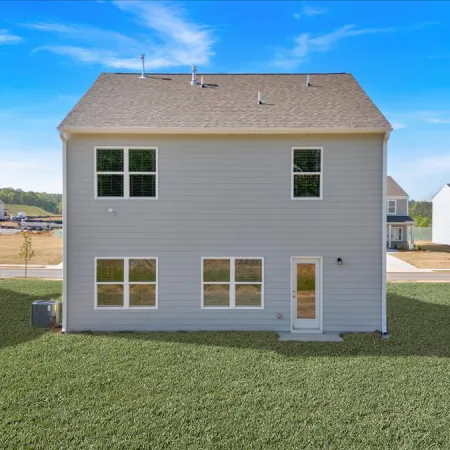 Back view of a two-story house with a spacious backyard and neighboring homes under a clear blue sky.
