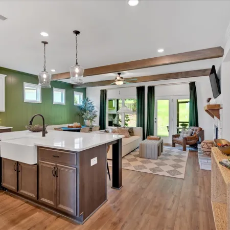 Open concept kitchen and living room with green accent wall, wooden beams, and modern farmhouse decor.