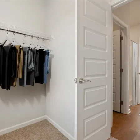 Minimalist closet with hanging clothes and open door leading to hallway and bedroom in modern home.