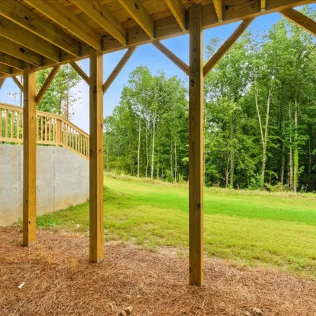 View from under a wooden deck showing support beams, a concrete wall, and green backyard with trees beyond.