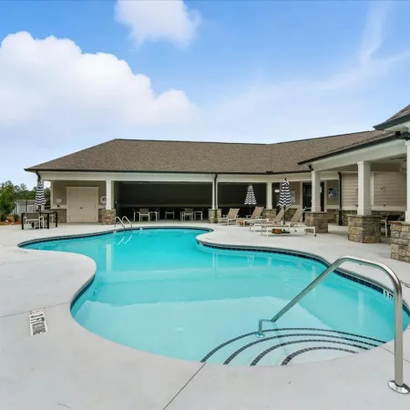 Outdoor swimming pool with lounge chairs and covered seating area under a blue sky at a residential complex.