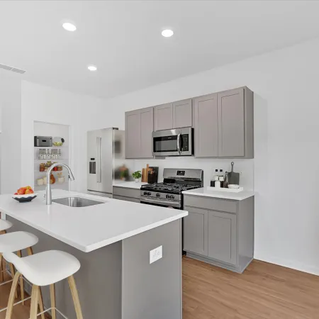 Modern kitchen with gray cabinetry, white countertops, and bright lighting, featuring a plant and breakfast bar.