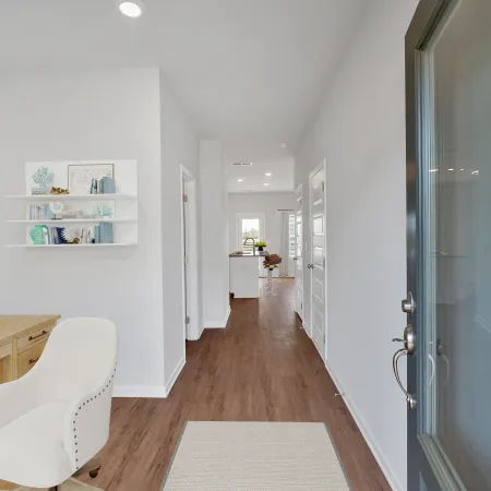 Modern white hallway with wood floors, desk workspace with chair, and open door revealing bright interior.