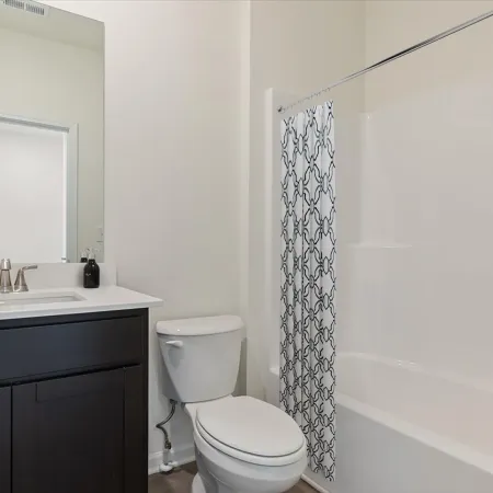 Modern bathroom with dark vanity, white toilet, large mirror, and bathtub with patterned shower curtain.
