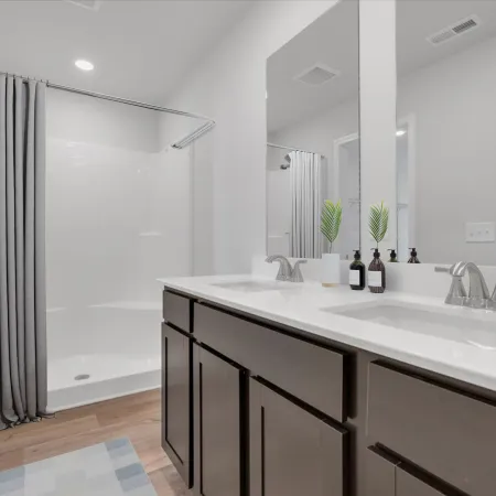Modern bathroom with double sink vanity, dark wood cabinets, walk-in shower, gray curtain, and large mirror.