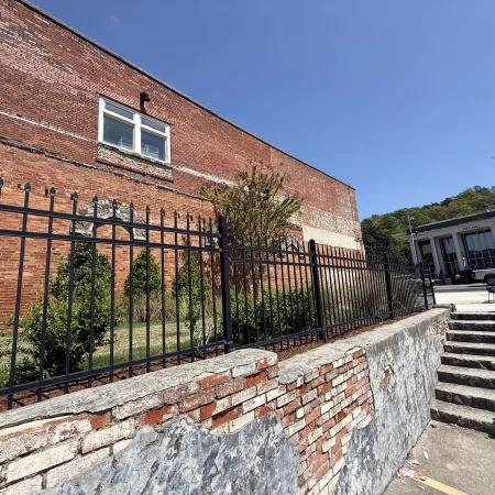 Historic brick building with a wrought iron fence and green landscape on a sunny day.