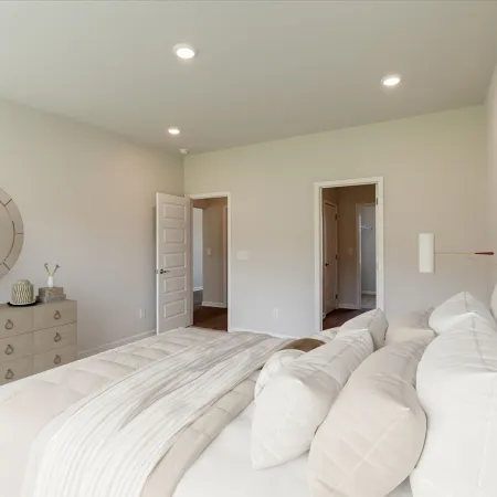 Bright modern bedroom with white bedding, round mirror, dresser, and colorful abstract wall art under recessed lighting.