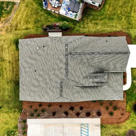 Aerial view of a suburban house with gray roof, surrounding yard, driveway, and nearby street.