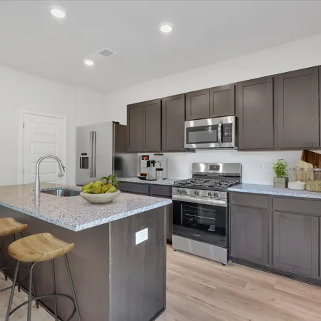 Modern kitchen with dark cabinets, granite countertops, stainless steel appliances, and wooden bar stools.
