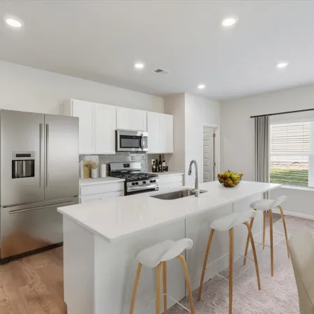 Modern kitchen with white cabinetry, stainless steel appliances, large island, and bar stools under recessed lighting.