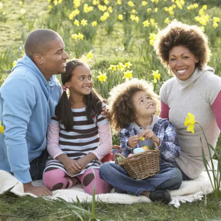 Happy family enjoying a spring day, sitting together in a field of blooming daffodils with a basket.