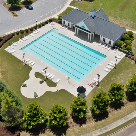Aerial view of an outdoor swimming pool with lanes, surrounded by lounge chairs, trees, and a clubhouse.