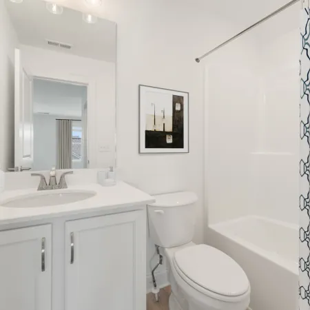 Bright white bathroom with sink, toilet, bathtub, patterned shower curtain, and framed wall art.