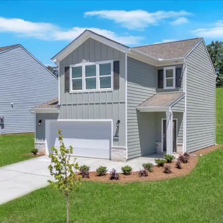 Modern two-story grey house with white trim, driveway, small landscaped garden, and green lawn under blue sky.