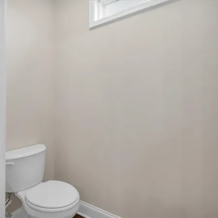Small clean bathroom with white toilet and beige walls under a small high window.