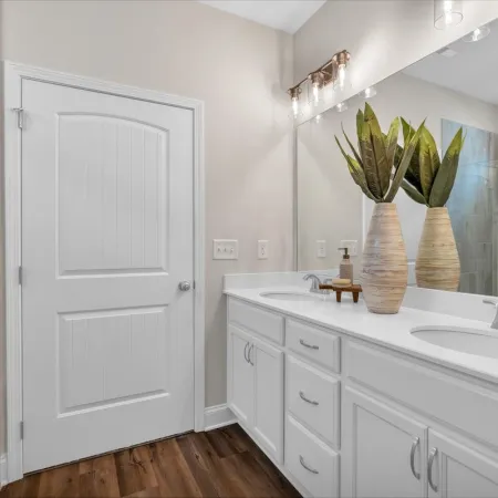 Modern bathroom with double sink white vanity, large mirror, glass shower, and wooden floor