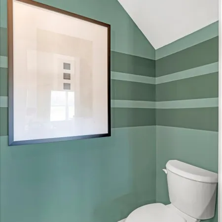 Stylish bathroom with green striped walls and framed artwork above a white toilet.