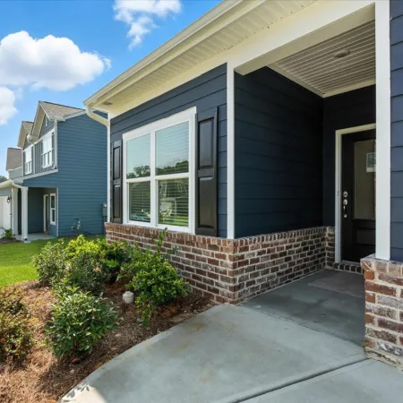 Exterior view of a modern blue house with brick accents, front porch, and well-maintained landscaping under a blue sky.