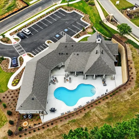 Aerial view of a residential complex with a uniquely shaped swimming pool, parking lot, and landscaped surroundings.