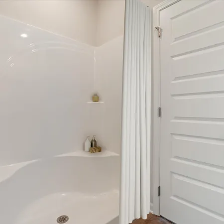 Clean white bathtub with built-in shelves holding toiletries next to a modern white paneled door with silver handle.