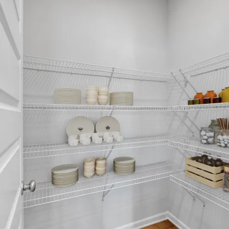 Organized pantry with white wire racks holding plates, mugs, jars, and bottles in a clean white room.