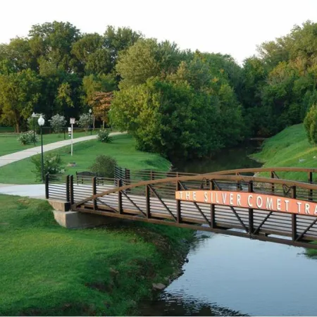 The Silver Comet Trail pedestrian bridge over a calm creek surrounded by green trees and walking paths in a park.