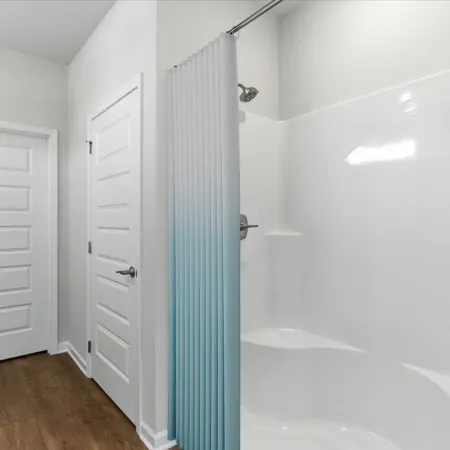 Minimalist bathroom with white shower, blue fade shower curtain, wood floor, and two white paneled doors.