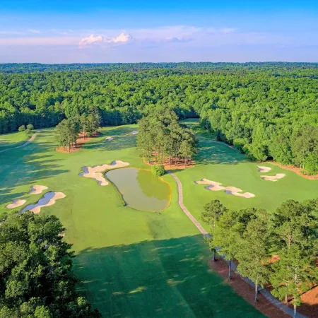 Aerial view of a golf course with sand bunkers, a water hazard, and lush green trees under a blue sky.