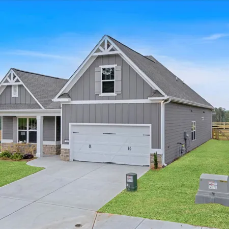 Modern gray suburban house with a two-car garage, manicured lawn, and clear blue sky in background.