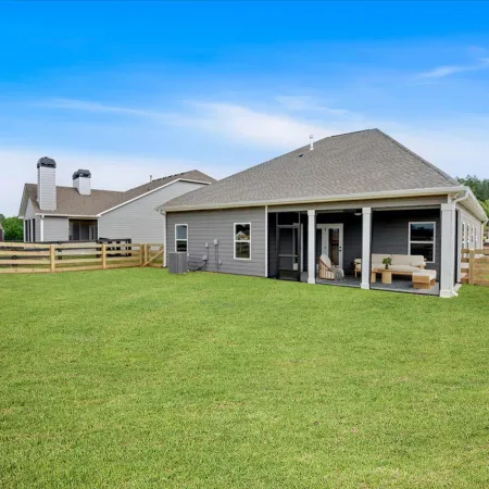 Spacious backyard with green lawn and wooden fence behind a modern gray house under a clear blue sky