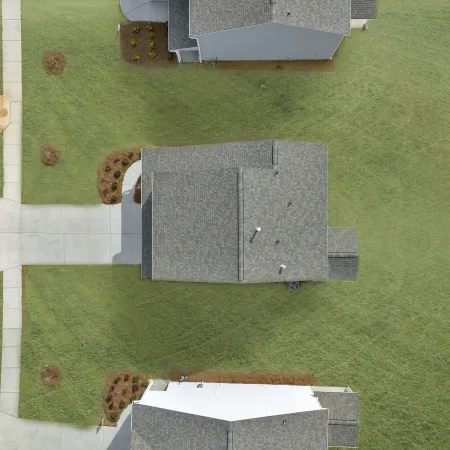 Aerial view of residential homes with green lawns and sidewalks in a suburban neighborhood.