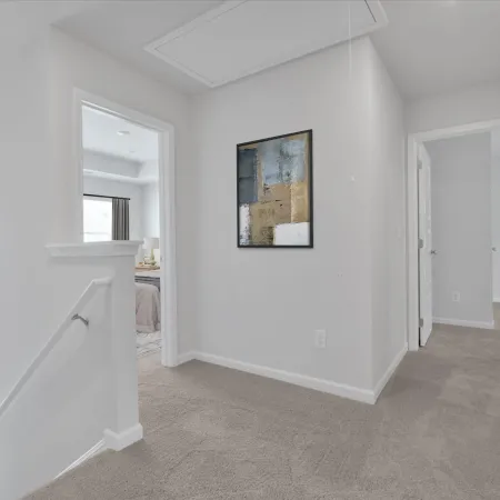 Bright hallway with beige carpet, white walls, staircase, doors, and abstract painting on wall