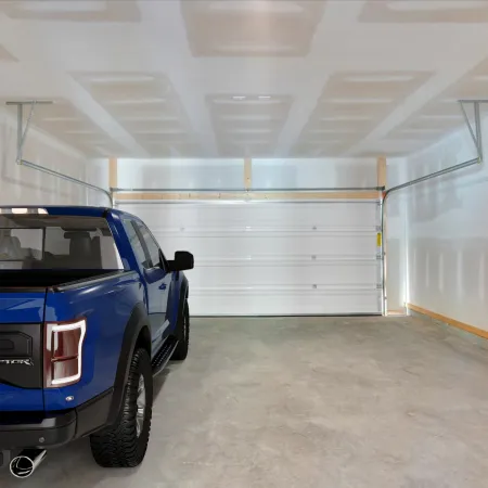 Blue pickup truck parked inside an empty, unfinished white garage with concrete floor and closed door.