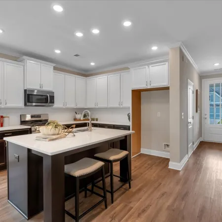 Modern kitchen with white cabinets, black island with stools, stainless steel appliances, and wood flooring.