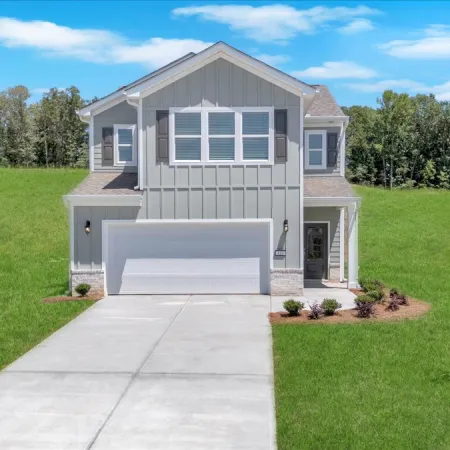 Modern two-story gray house with white garage door, concrete driveway, green lawn, and blue sky background.