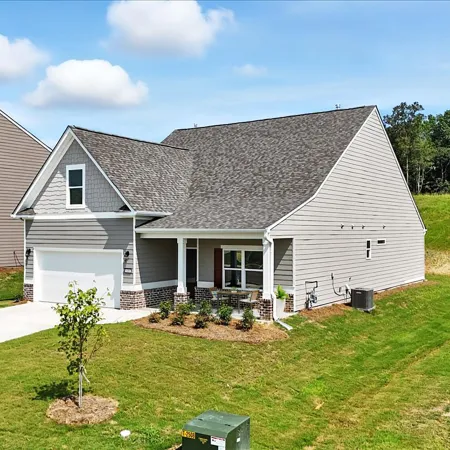 New suburban single-story gray house with a garage, front porch, and green lawn under blue sky with clouds.