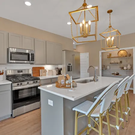 Modern kitchen featuring gray cabinets, white countertops, and stylish golden pendant lights.
