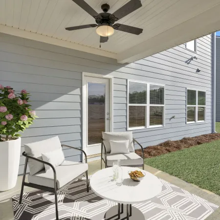 Cozy outdoor patio with seating, table and decorative plant, surrounded by a green lawn.