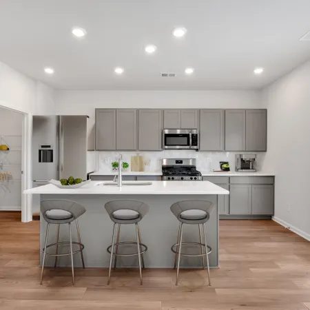 Modern kitchen with gray cabinets, stainless steel appliances, island with three stools, and wood flooring