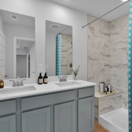 Modern bathroom with double sink vanity, large mirror, marble tiled shower, and teal patterned curtain
