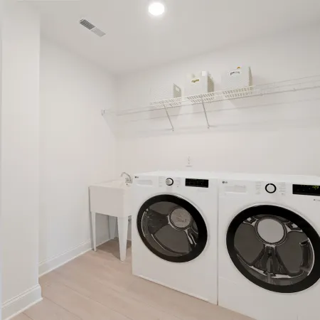 Bright laundry room with white front-load washer and dryer, utility sink, and wire shelf with storage baskets.