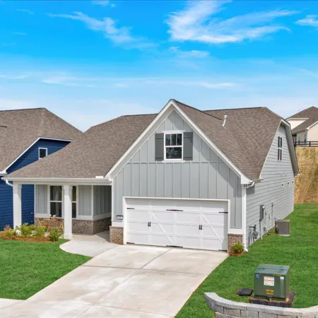 Modern suburban homes with green lawns, driveways, and clear blue sky in a residential neighborhood.