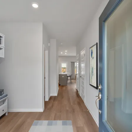 View of a modern entryway with a blue door, white walls, wooden floor, and hallway leading to a kitchen area.