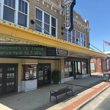 Historic brick theater building with yellow marquee, digital sign, and American flag on clear blue sky day.