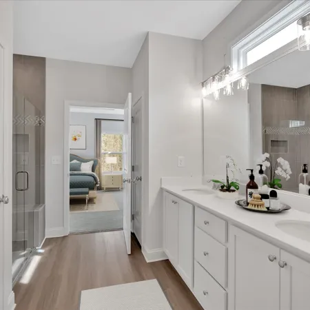 Modern bathroom with double vanity, large mirror, glass shower, and view into adjacent bedroom